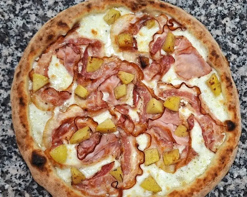 La pizza Botero sul piano di granito: mozzarella, fette di porchetta e cubetti di patate al forno