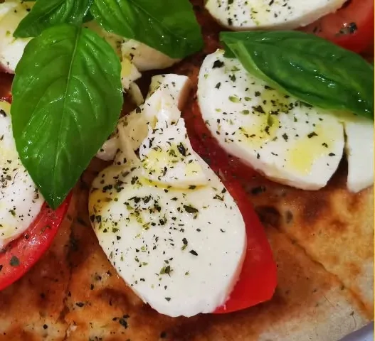 Focaccia caprese con fette di pomodoro, mozzarella, basilico e origano
